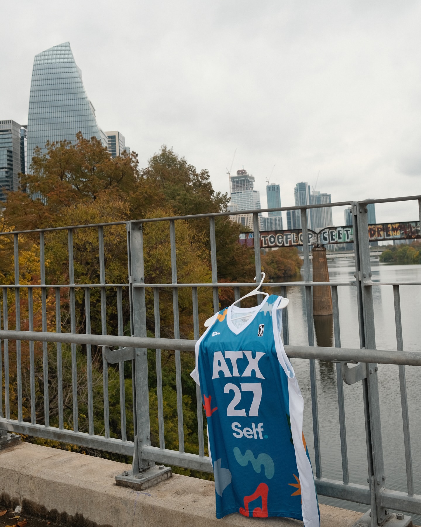 Basketball jersey hangs on bridge in Austin, Texas, featuring the ATX logo, set against the backdrop of city skyline and river.