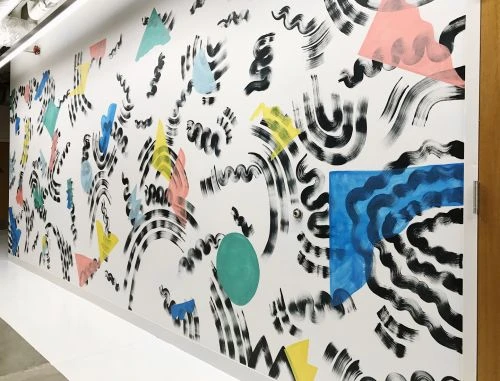 White wall featuring abstract art with black brush strokes and geometric shapes in yellow, pink, blue, and green, creating a bold design.