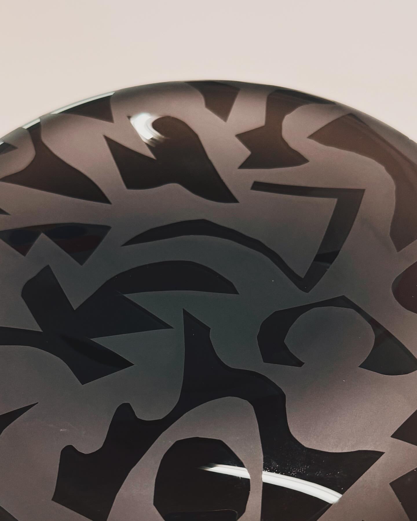 Abstract art bowl with grey and black tones, showcasing a unique pattern and design against a bright white backdrop in dim lighting.