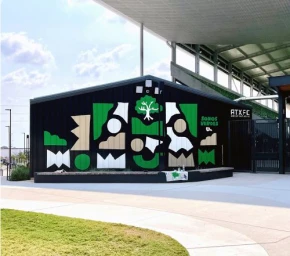 Large geometric mural with green, white, and tan shapes and a tree icon on a black building exterior by illustrator Will Bryant