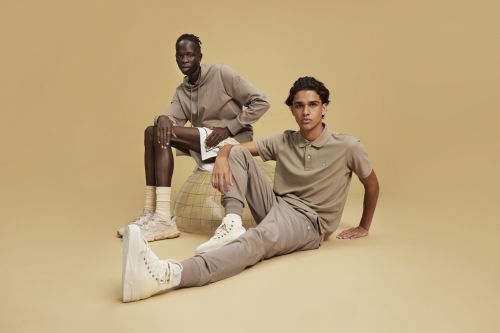 Two models pose in casual, neutral-toned outfits against a plain backdrop, showcasing modern fashion and minimalist style in a studio setting.
