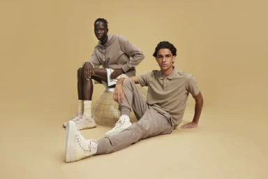 Two male models in neutral tone sportswear posing against a warm beige seamless studio backdrop in Los Angeles.