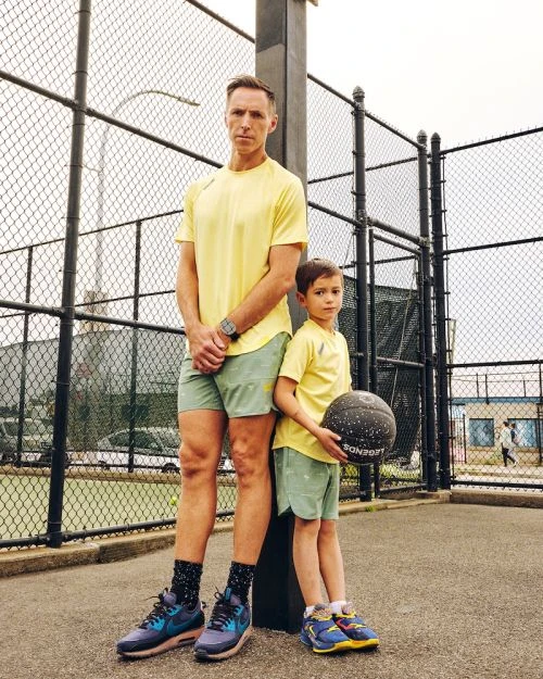 Adult male and child in matching outfits posing on an outdoor basketball court, dressed in sport attire, with a ball, sunny day.
