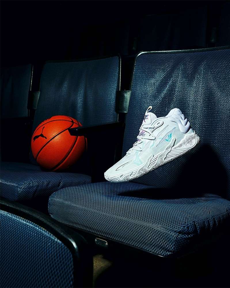A white basketball shoe is placed on the seat of an empty theater, with an orange Puma basketball in the background, creating a dynamic scene.