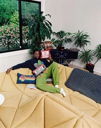 Man lounging on a large yellow sectional sofa surrounded by potted plants in a bright interior by photographer David Cabrera.