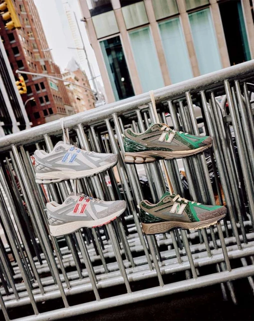 Four New Balance sneakers hang on a metal barricade against an urban backdrop, showcasing a unique product display in an outdoor setting.