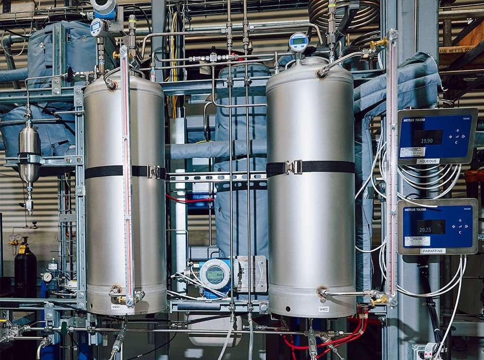 Industrial setup featuring two large stainless steel tanks, gauges, pipes, and monitoring devices in a complex arrangement, indoors.
