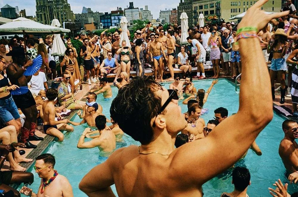 Large group of people enjoying a rooftop pool party in the city, with buildings in the background and a sunny daytime atmosphere.