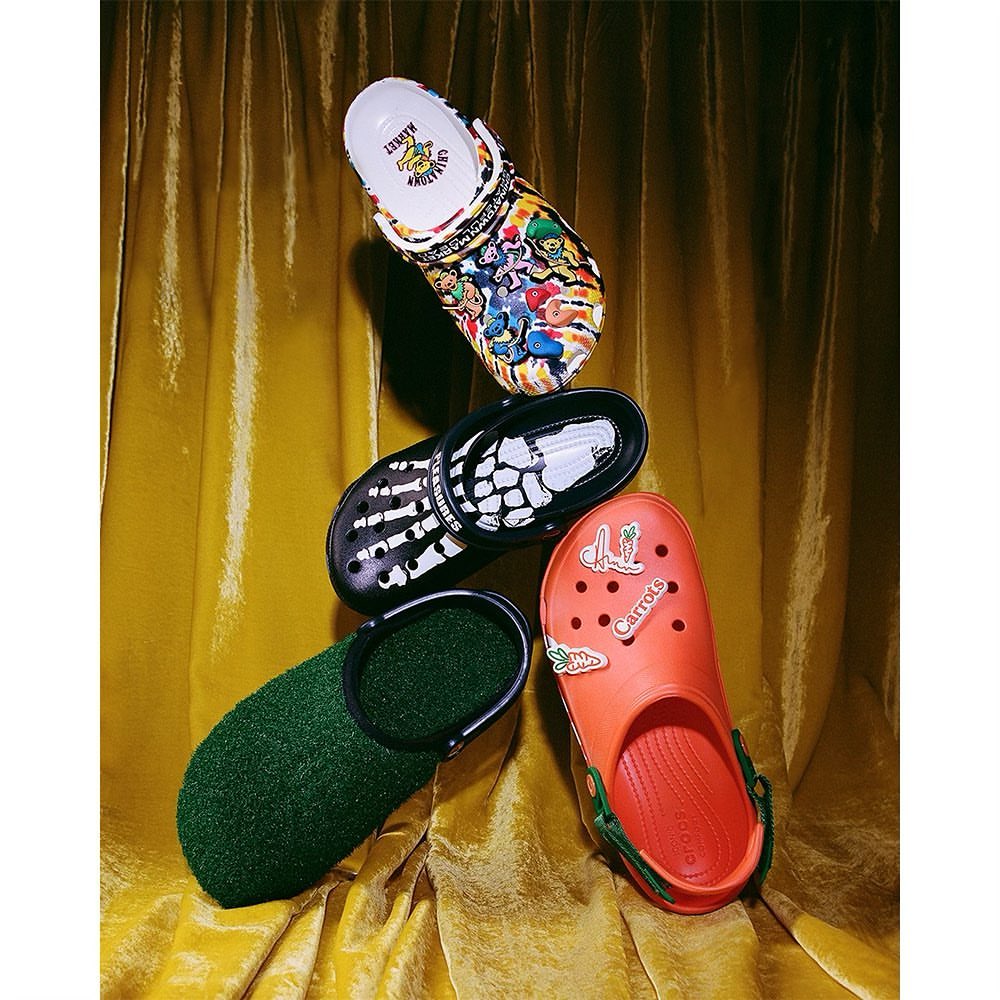Four Crocs clogs in a vertical composition against a golden, shimmering curtain backdrop. Each clog has a unique design.