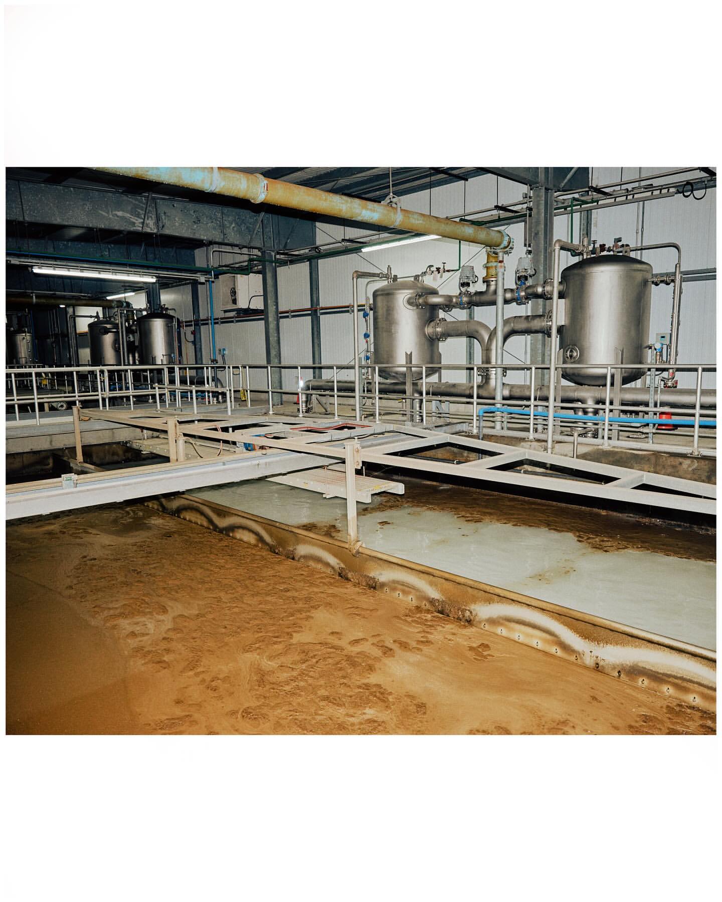 Industrial processing plant interior with stainless steel tanks, pipes, and metal structures, showcasing a large, open room.