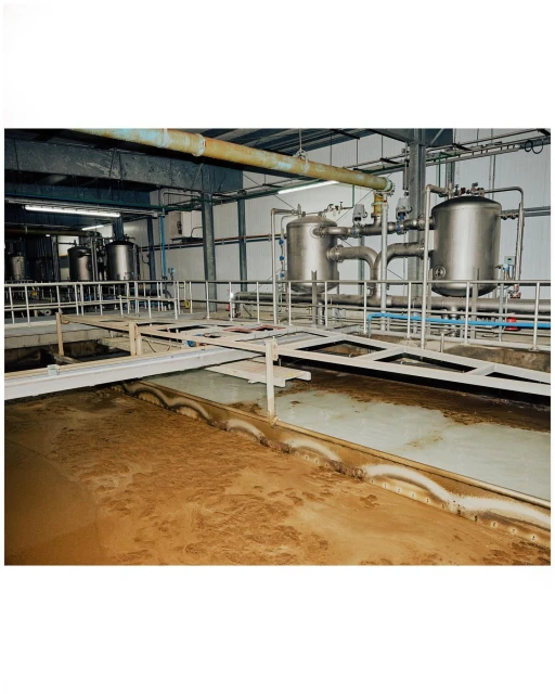 Industrial processing plant interior with stainless steel tanks, pipes, and metal structures, showcasing a large, open room.