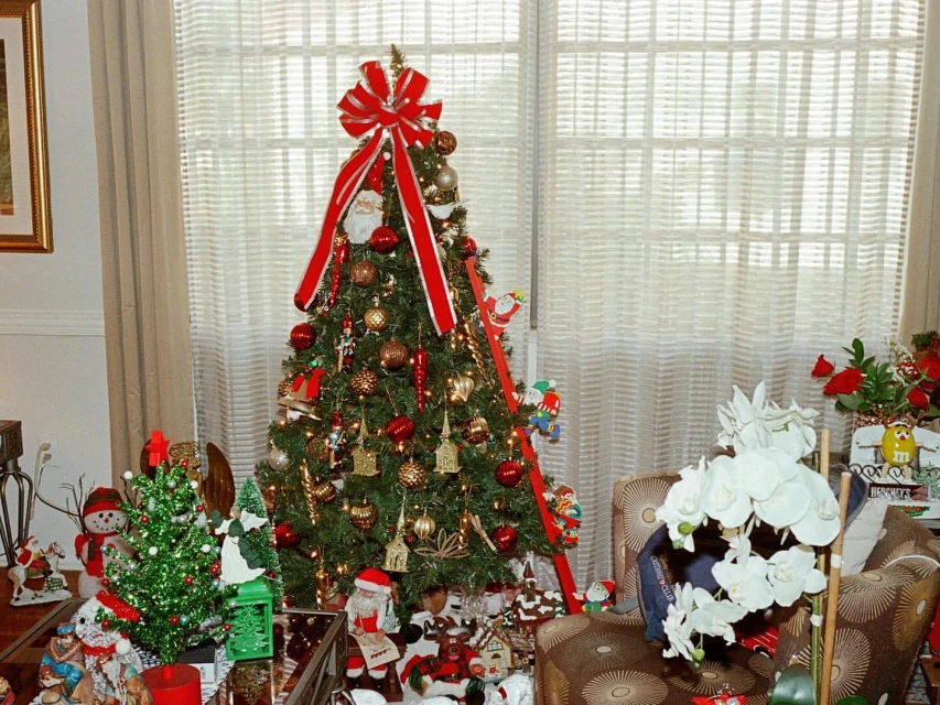 Christmas tree decorated with ornaments, red ribbon, and Santa figure indoors near windows, creating a festive holiday atmosphere.