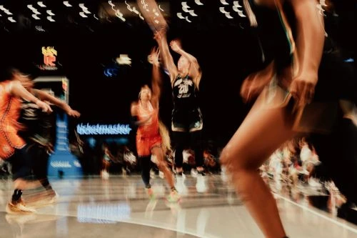 A blurred action shot of women's basketball game with players in action and the Ticketmaster logo visible in the background.