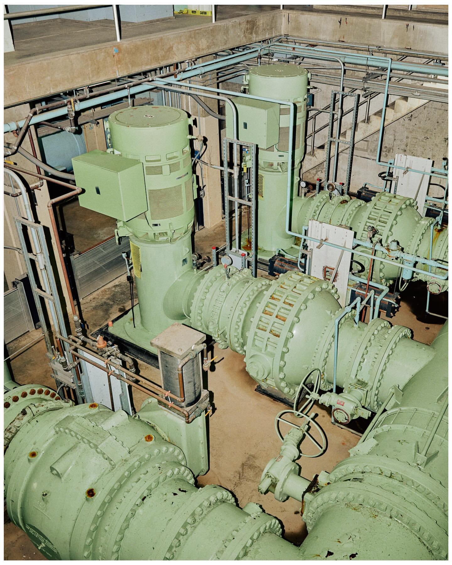 Industrial interior featuring large, light green machinery with pipes and valves against a concrete wall, showing engineering elements.