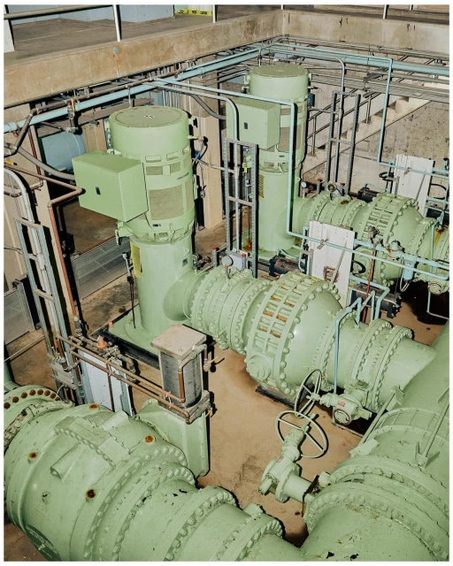 Industrial interior featuring large, light green machinery with pipes and valves against a concrete wall, showing engineering elements.