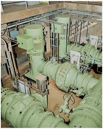 Industrial interior featuring large, light green machinery with pipes and valves against a concrete wall, showing engineering elements.