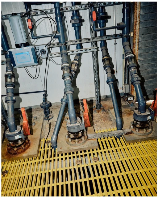 Industrial pipes and valves connect to machinery on a yellow platform with a white wall in the background.