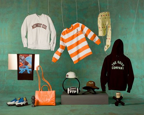 Display of clothing, accessories, and objects suspended against a textured green wall in a studio setting with soft, diffused lighting.