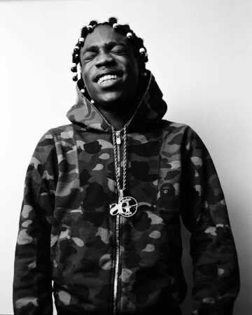 Black and white portrait of a smiling African American man wearing a camouflage hooded jacket and a pendant necklace.