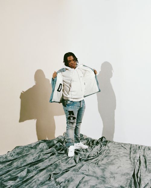 Young man in hoodie and jeans standing on draped surface in studio. Casual fashion shoot featuring modern streetwear and neutral background.