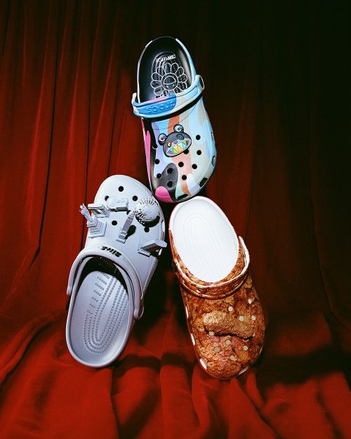 Three pairs of Crocs clogs arranged against a backdrop of draped red velvet fabric in a studio setting, showcasing their unique designs.