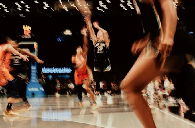 Women's basketball game in arena with fast action, players in blurred motion competing for the ball on a shiny court.