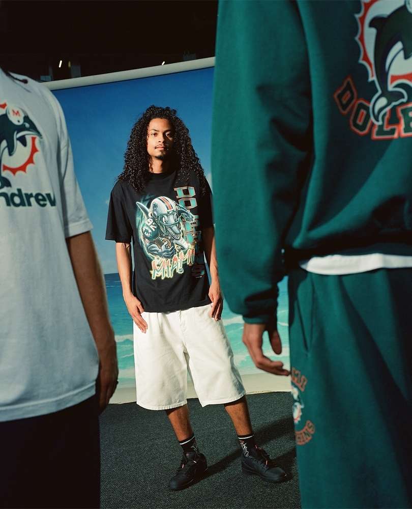 Three people pose in a photo studio wearing Miami Dolphins themed apparel in a medium shot with a beach backdrop.