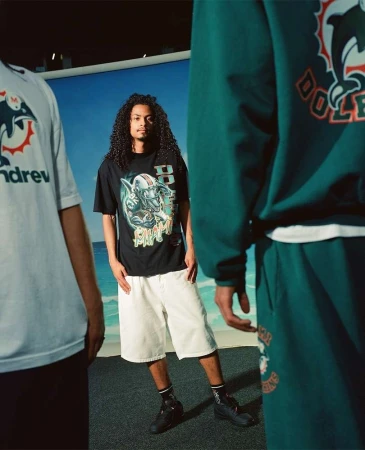 Three people pose in a photo studio wearing Miami Dolphins themed apparel in a medium shot with a beach backdrop.