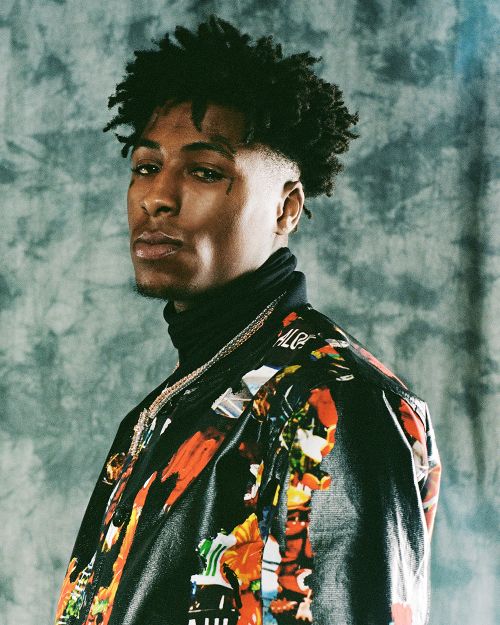 Portrait of a young African-American man with curly hair wearing a turtleneck sweater and patterned jacket against a mottled background.
