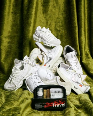 Pile of white sneakers with a sneaker cleaning kit in front of a green velvet curtain backdrop, showcasing sneaker culture.