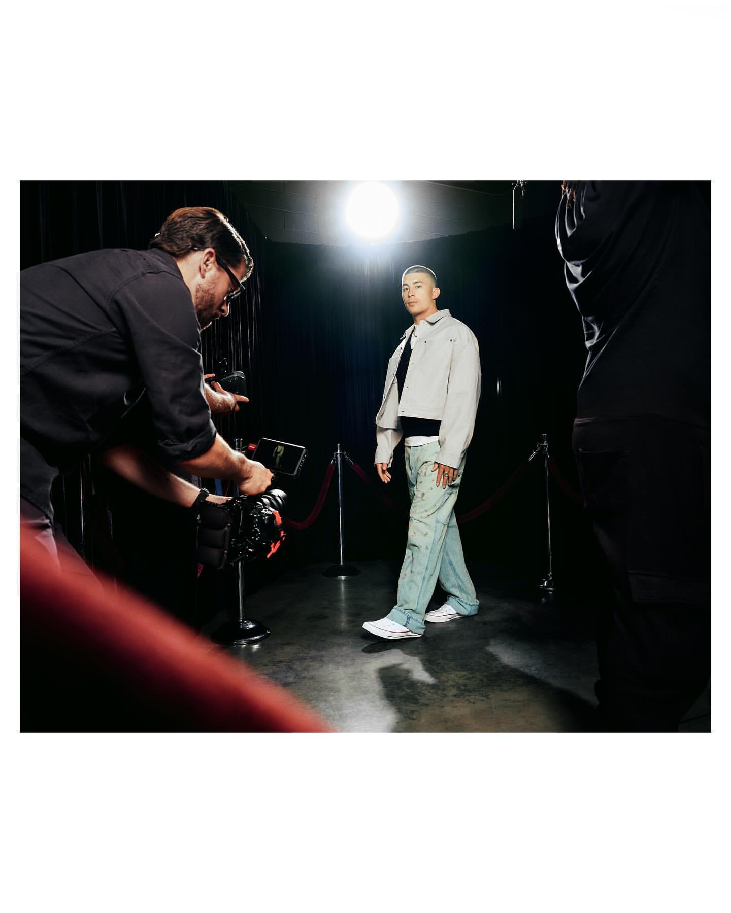 Young man walks the red carpet as a cameraman captures the moment in a studio setting with bright lighting.