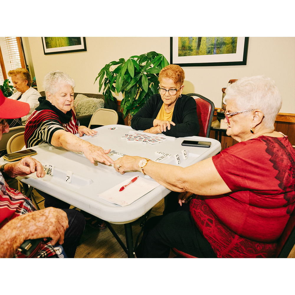 Group of senior women and men play dominoes at a table indoors. Elderly people are sitting and enjoying a game with domino tiles.