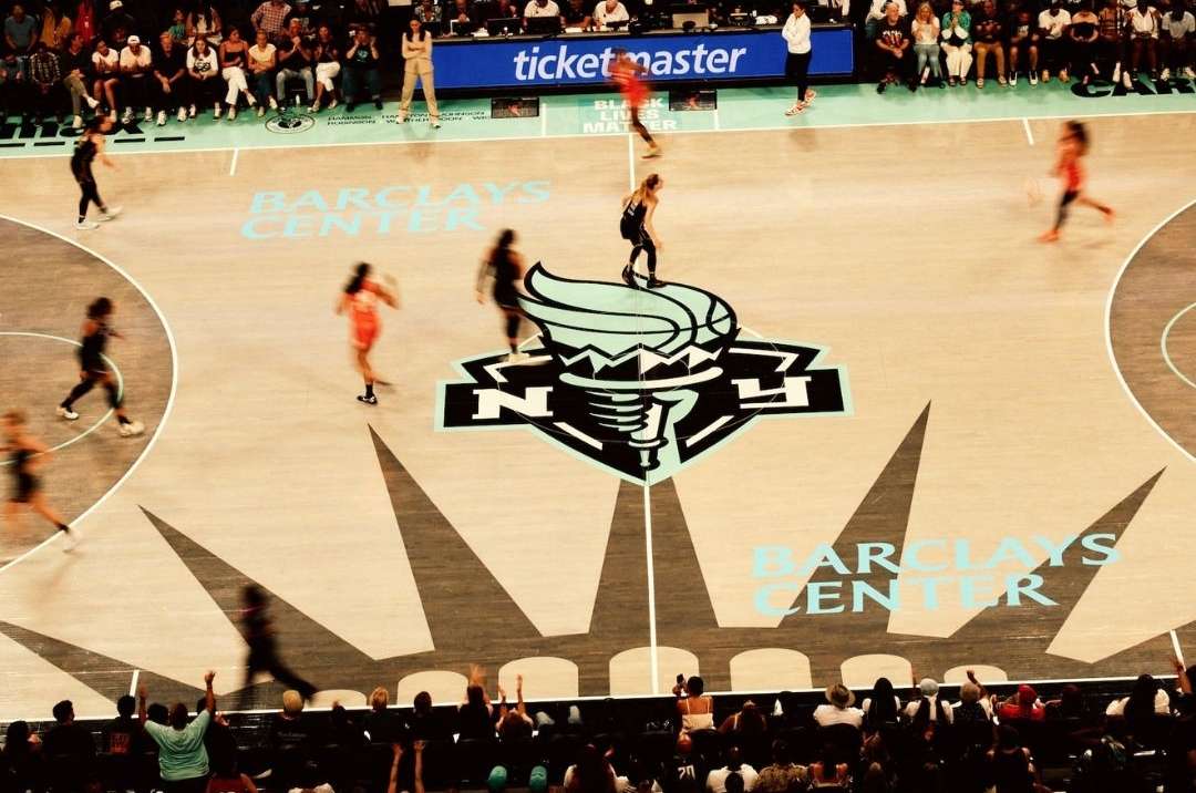 Basketball game at Barclays Center featuring players in action, crowd in background, and the team's logo on the court floor.