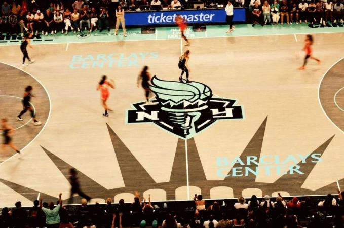 Basketball game at Barclays Center featuring players in action, crowd in background, and the team's logo on the court floor.