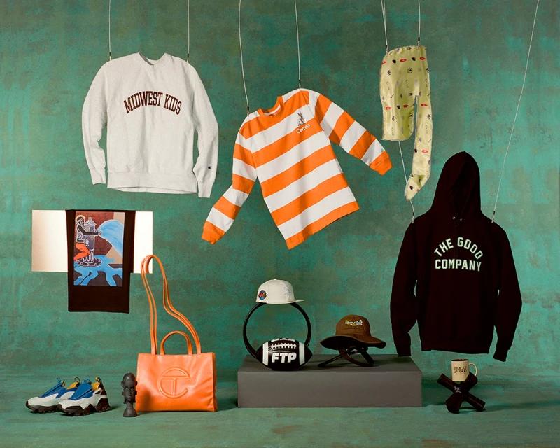 Still life shot of apparel and accessories hanging from strings, including sweatshirts, shirts, pants, hats, a handbag, and shoes.
