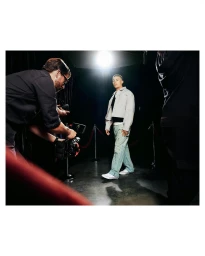 Photographer in a dark studio capturing a male model walking toward the camera under bright overhead lighting
