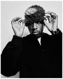 Black man wearing textured bucket hat adjusting it with both hands against a plain white studio background.
