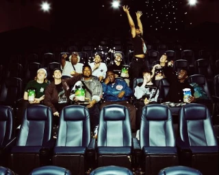 Group of diverse young friends sitting in a dark cinema auditorium eating popcorn with loose pieces flying through the air.