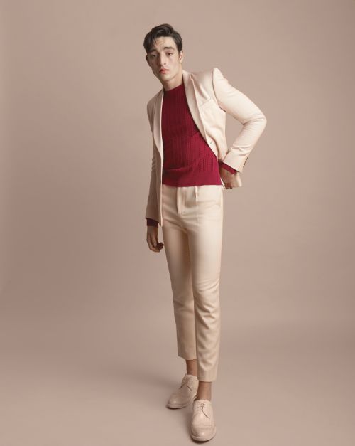 Full-length shot of an adult male wearing a light beige suit with a red sweater, posing in a photo studio setting. Fashion editorial.