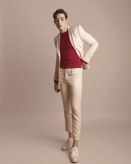 Full-length shot of an adult male wearing a light beige suit with a red sweater, posing in a photo studio setting. Fashion editorial.