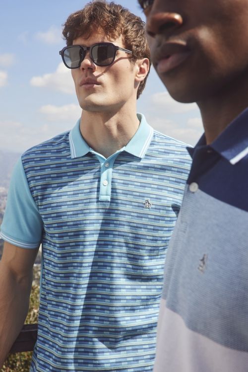 Two men outdoors wearing polo shirts and sunglasses on a sunny day, showcasing men's fashion with a blurred landscape background.