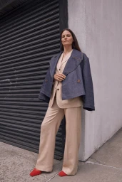 Woman in beige pantsuit and oversized denim jacket standing outdoors against a corrugated metal shutter in Los Angeles.