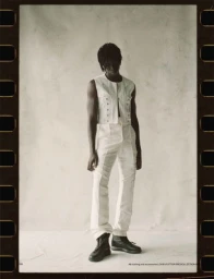 Full-length portrait of a male model wearing white vest and trousers against a textured background framed by film sprocket holes