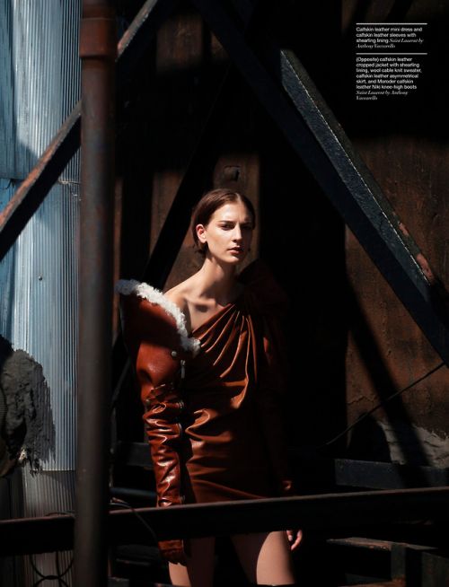 Fashion editorial shot of a woman in a brown leather dress with a fur collar, posing in an industrial setting with steel and rust.