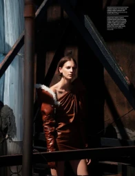 Model in brown leather dress with shearling trim posing near industrial beams with dramatic shadows