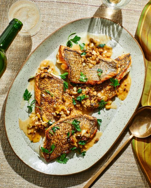 Overhead shot of fish fillets with sauce and parsley on an oval plate, accompanied by a wine bottle and glass. Culinary presentation.