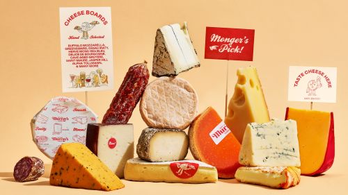 An assortment of cheeses and cured meats, including hard and soft cheeses, salami, and signage with food and promotional messaging.