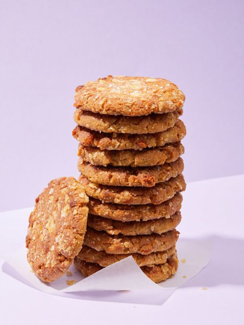 Stack of homemade oatmeal cookies on a white surface against a pale violet background. The cookies are golden brown.
