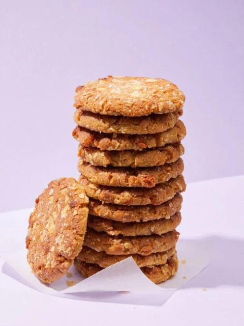 Stack of homemade oatmeal cookies on a white surface against a pale violet background. The cookies are golden brown.