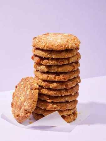 Stack of homemade oatmeal cookies on a white surface against a pale violet background. The cookies are golden brown.